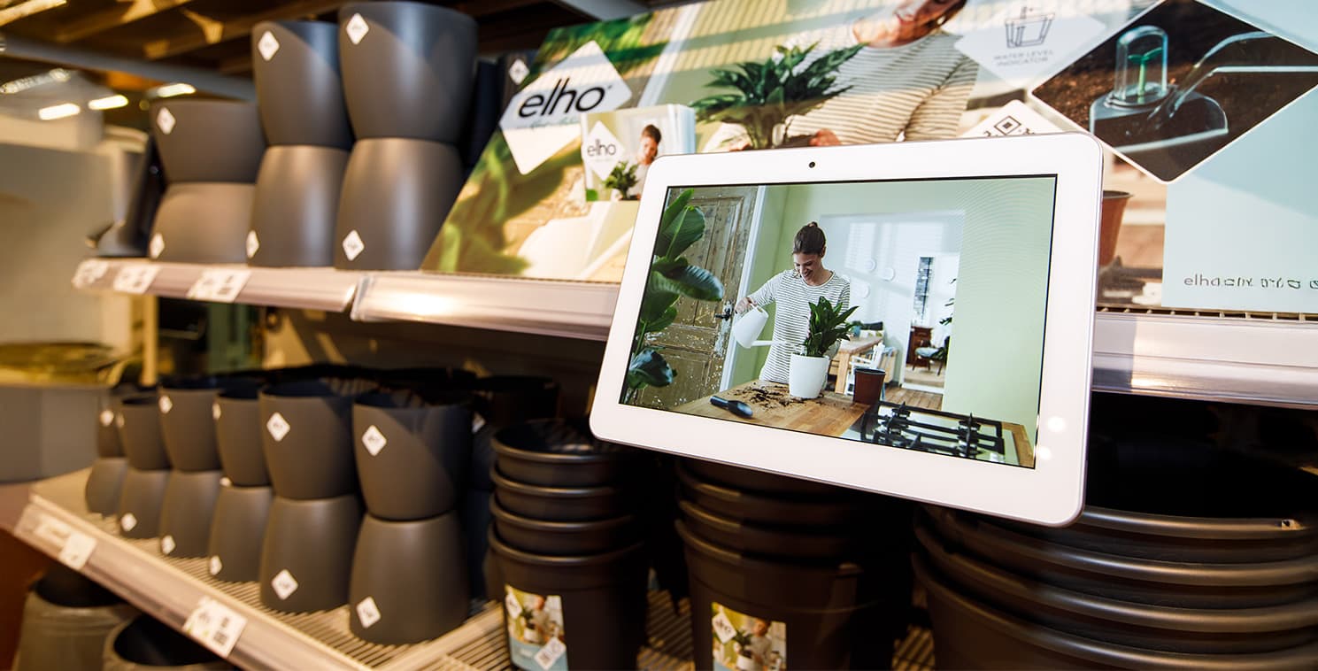 An Elo touchscreen mounted on a retail shelf shows a product demonstration video, providing interactive education to shoppers browsing in-aisle merchandise.